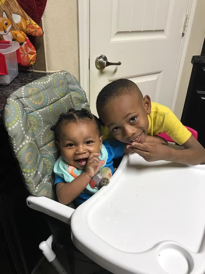 Child in high chair with another child leaning over