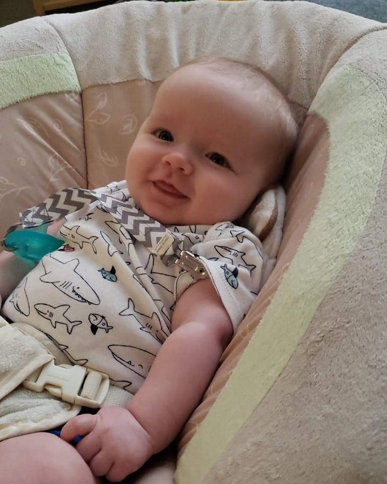 Child in a patterned shirt sitting in a bouncer