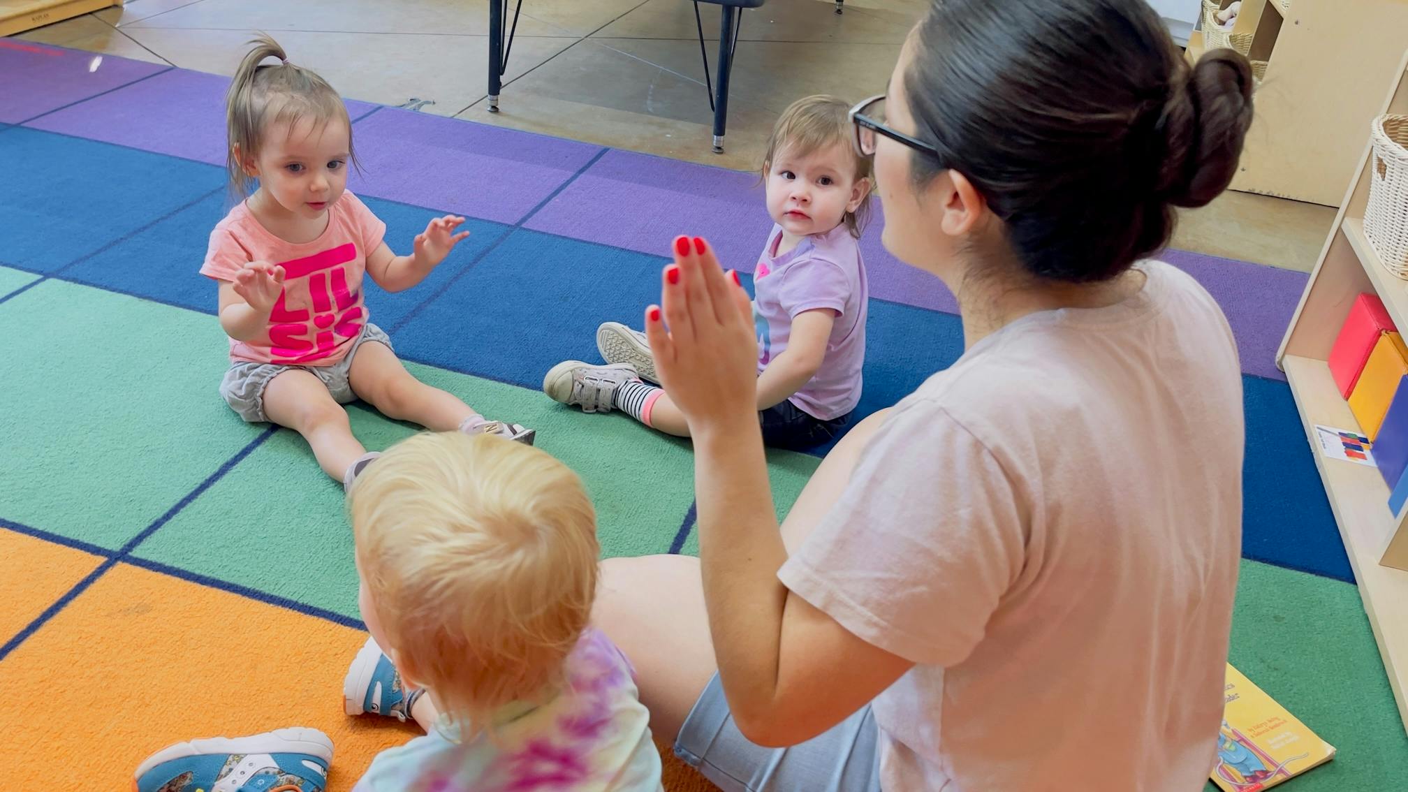 Adult and three children sitting on a colorful mat