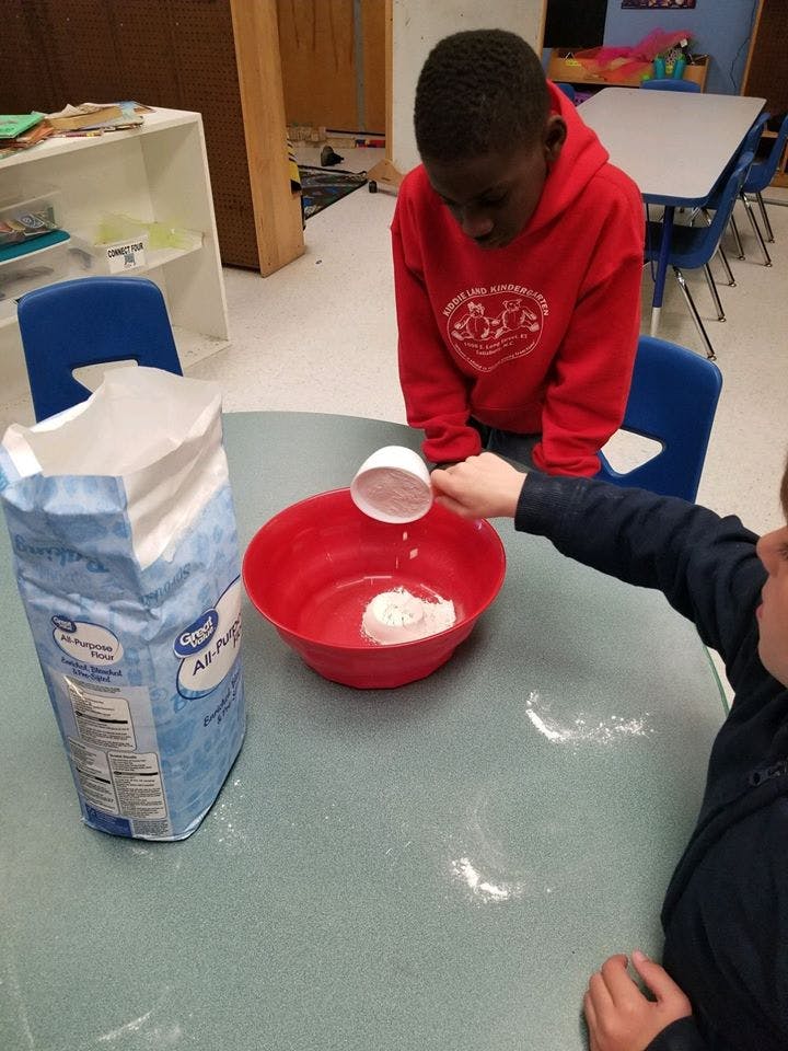 Child pouring flour from a measuring cup into a red bowl