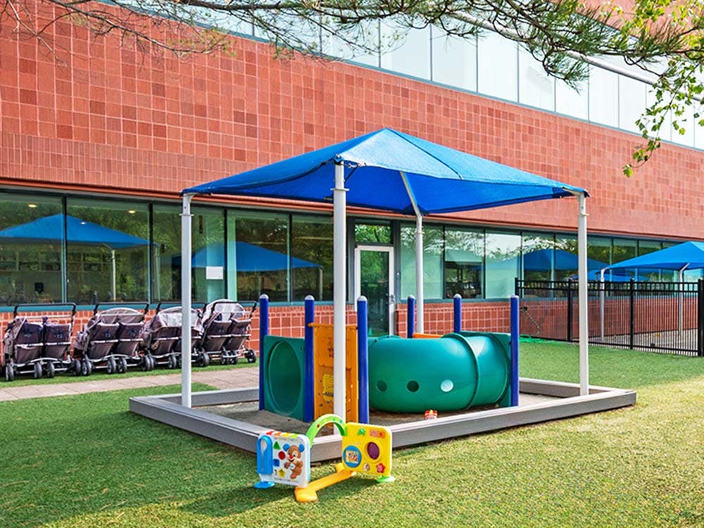 Outdoor play area with a blue canopy, sandbox, and toy tunnel