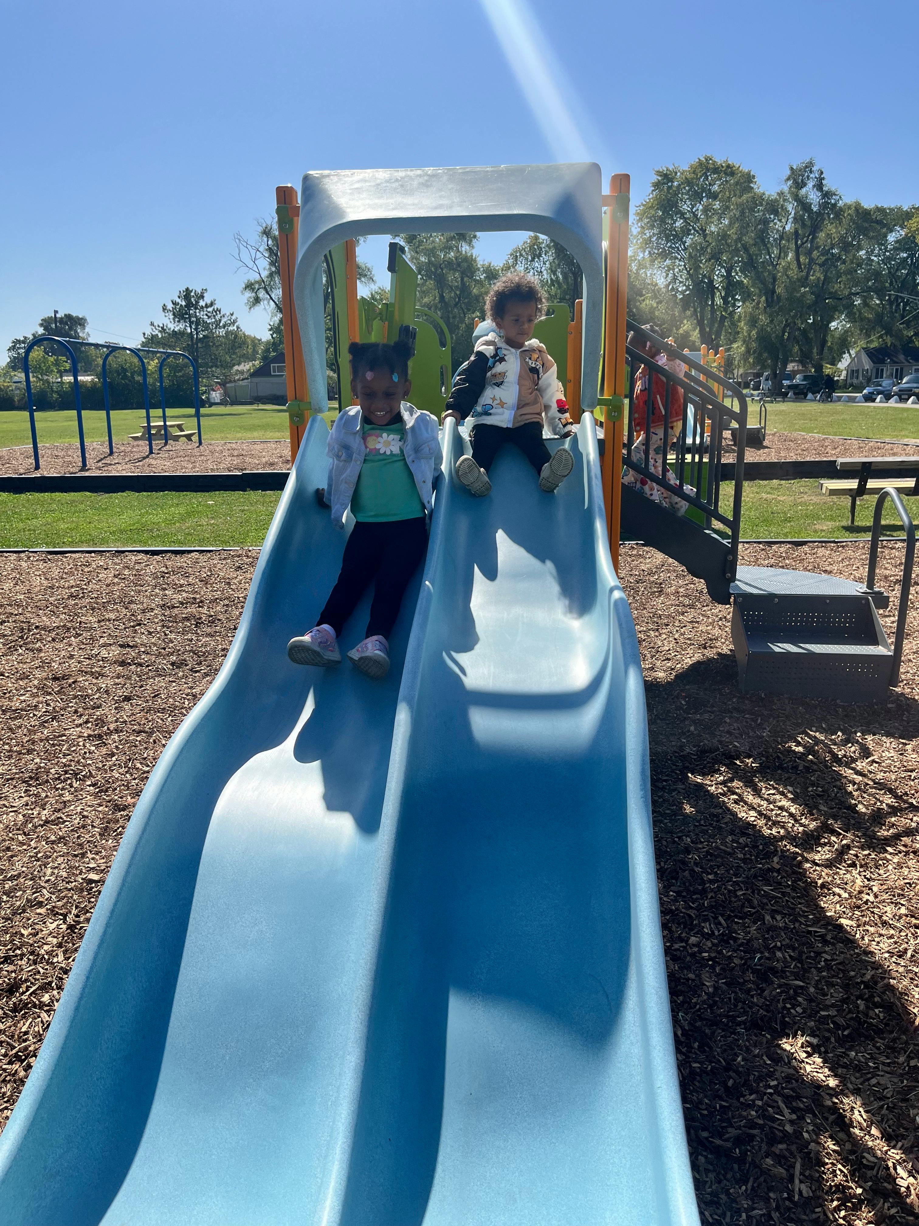 Two children sitting on a blue slide at a playground