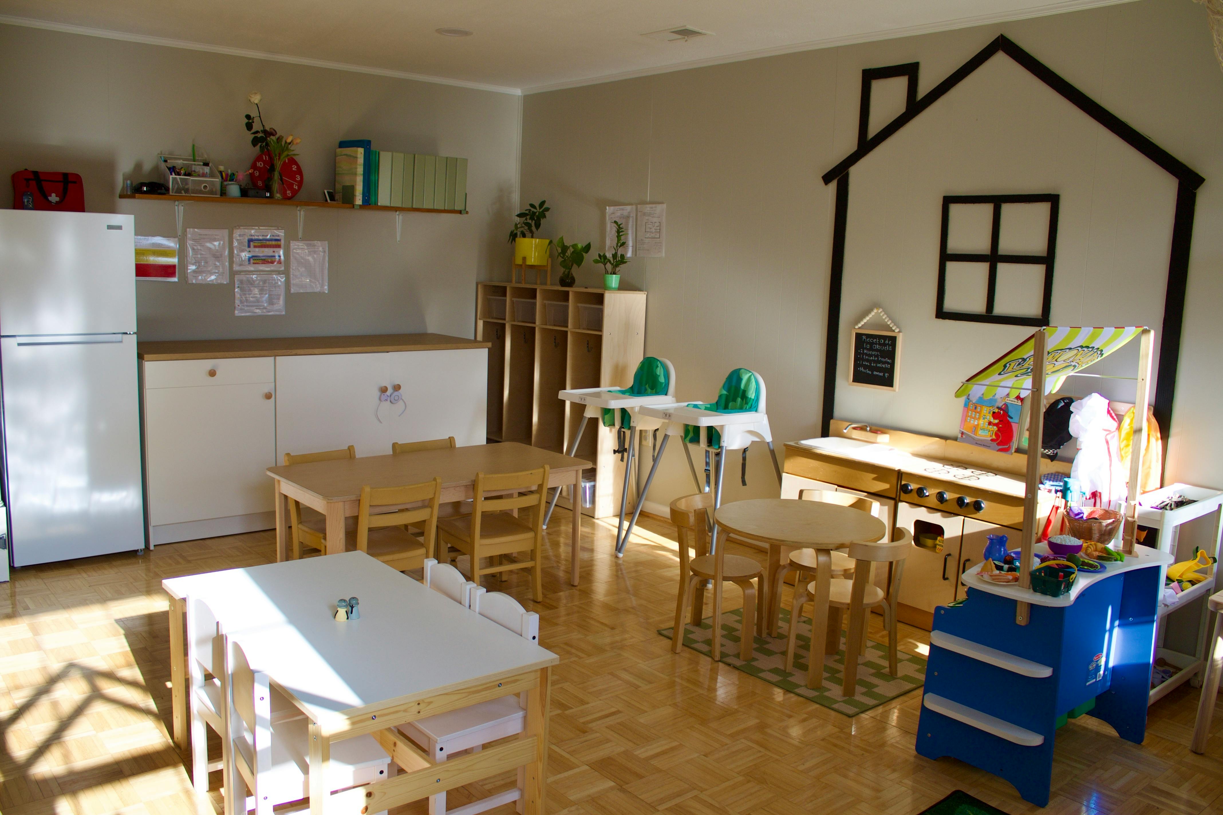 Empty classroom with small tables and chairs, and a house outline on the wall