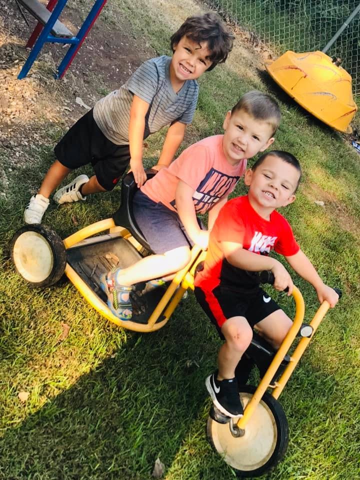 Three children playing on a yellow tricycle