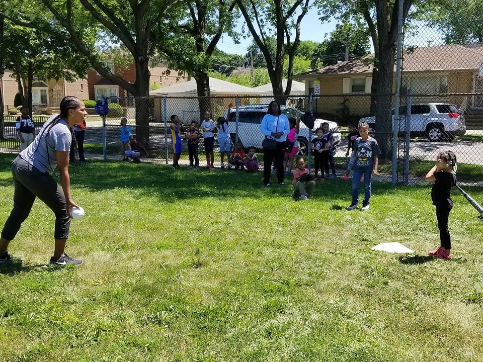 Person pitching a ball to a child holding a bat, with other people watching