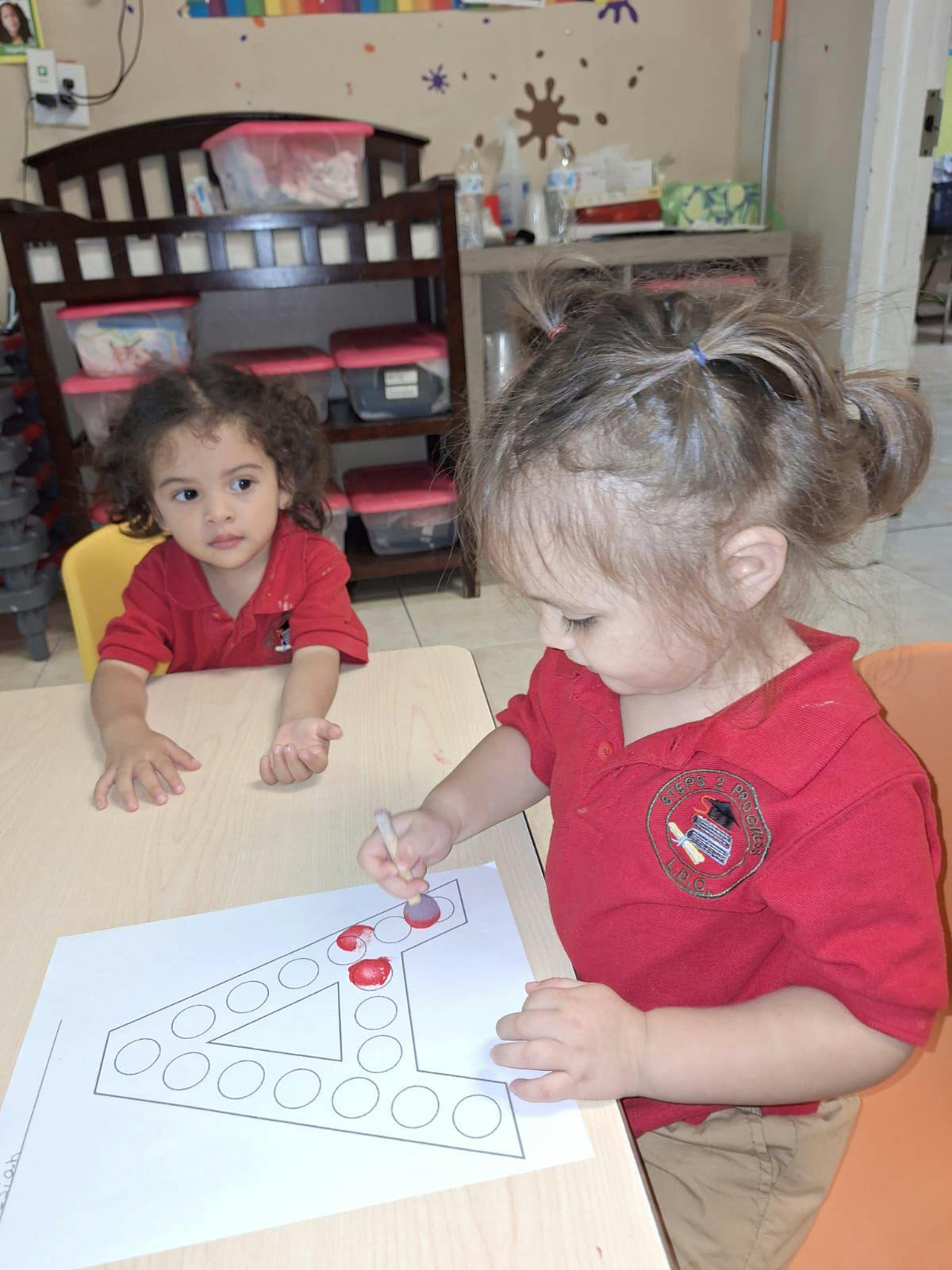 Two children at a table, one coloring a number four outline