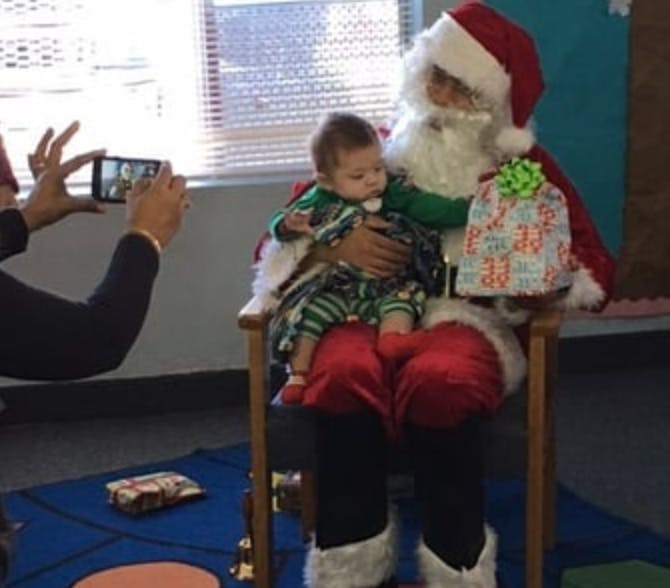 Person dressed as Santa holding a child while another person takes a photo
