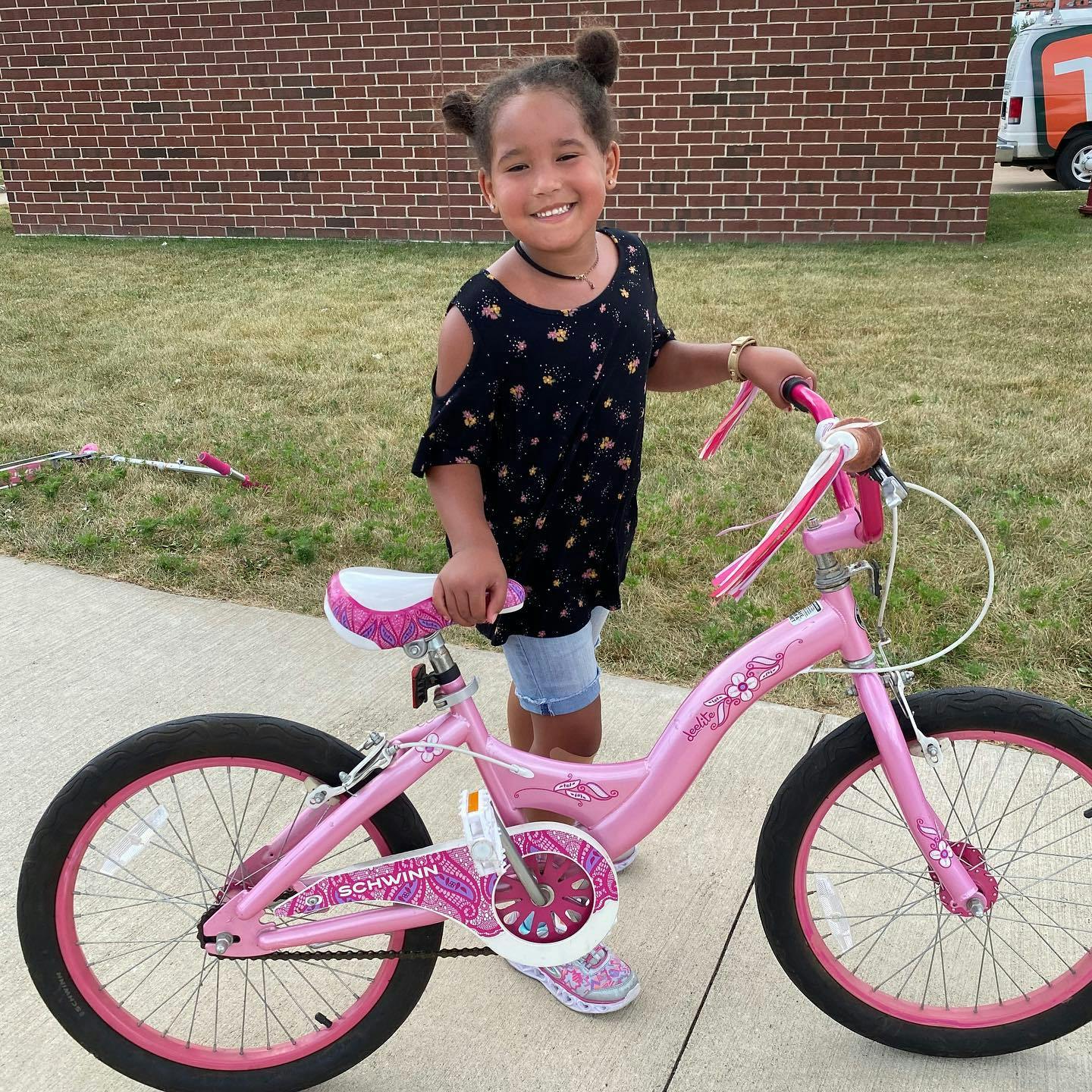 Child standing next to a pink bicycle