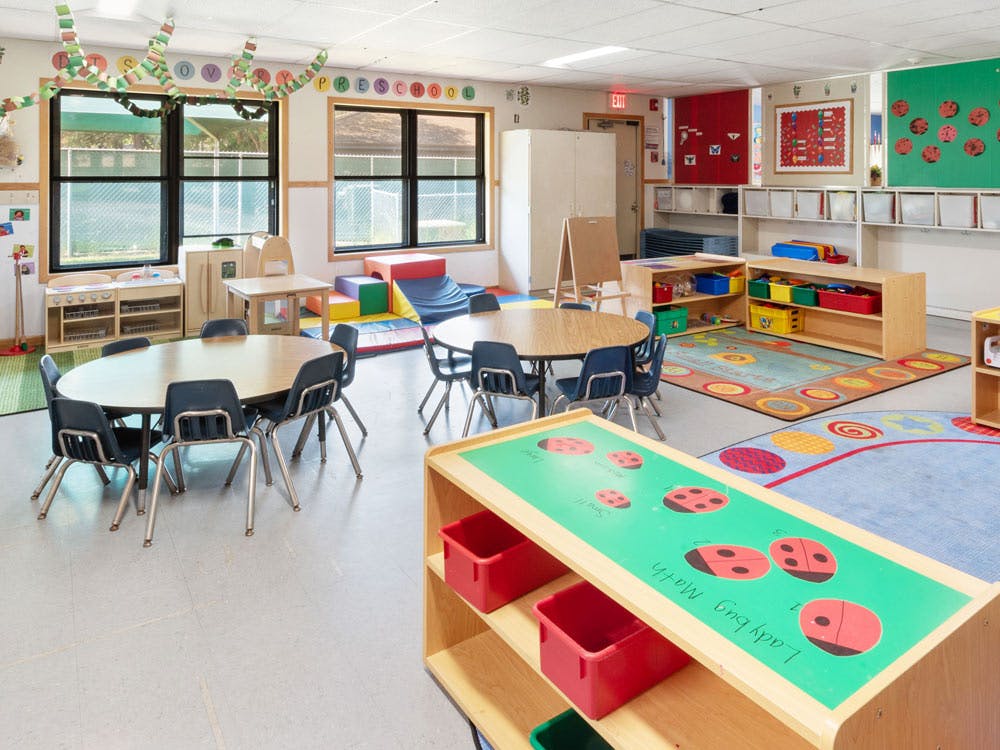 Empty preschool classroom with tables, chairs, and play equipment