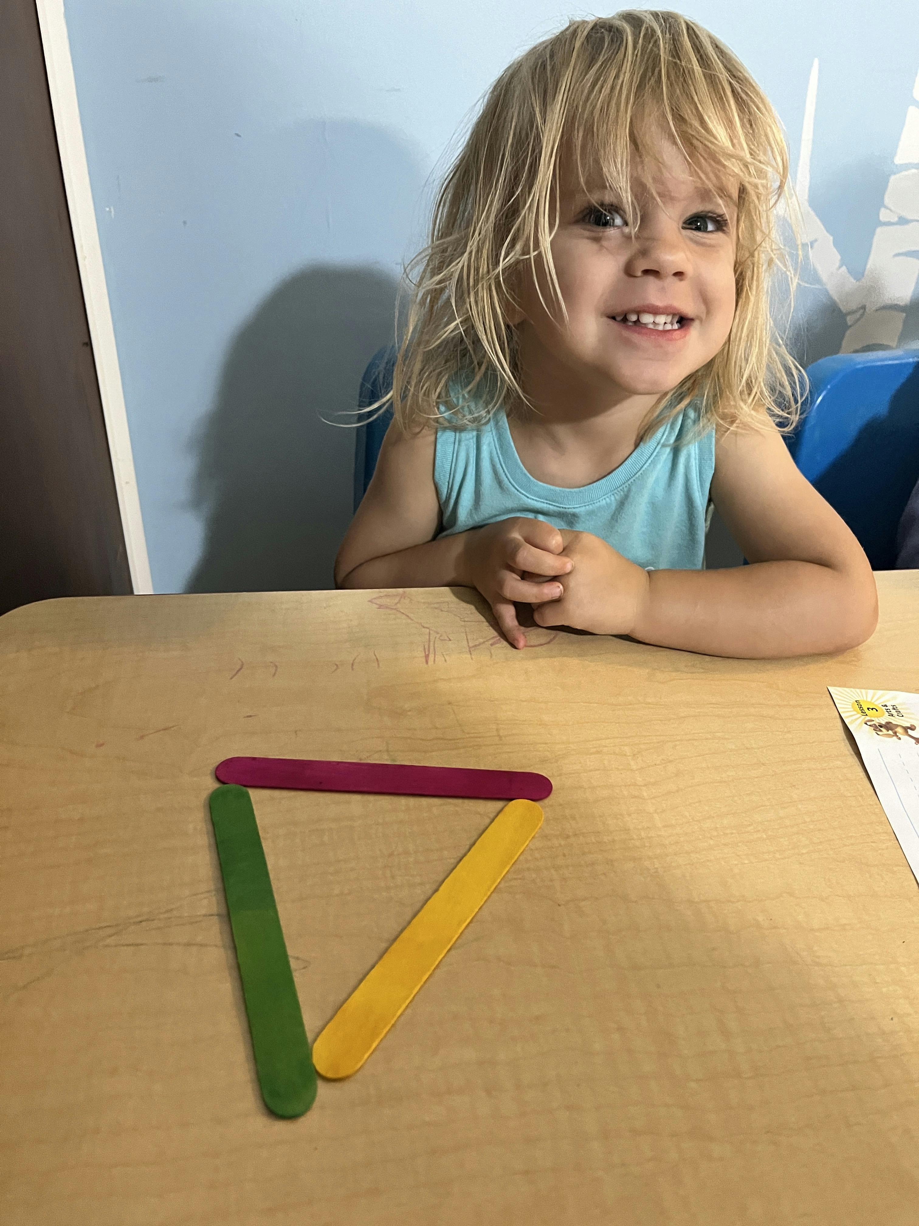 Child sitting at a desk with a triangle made of craft sticks