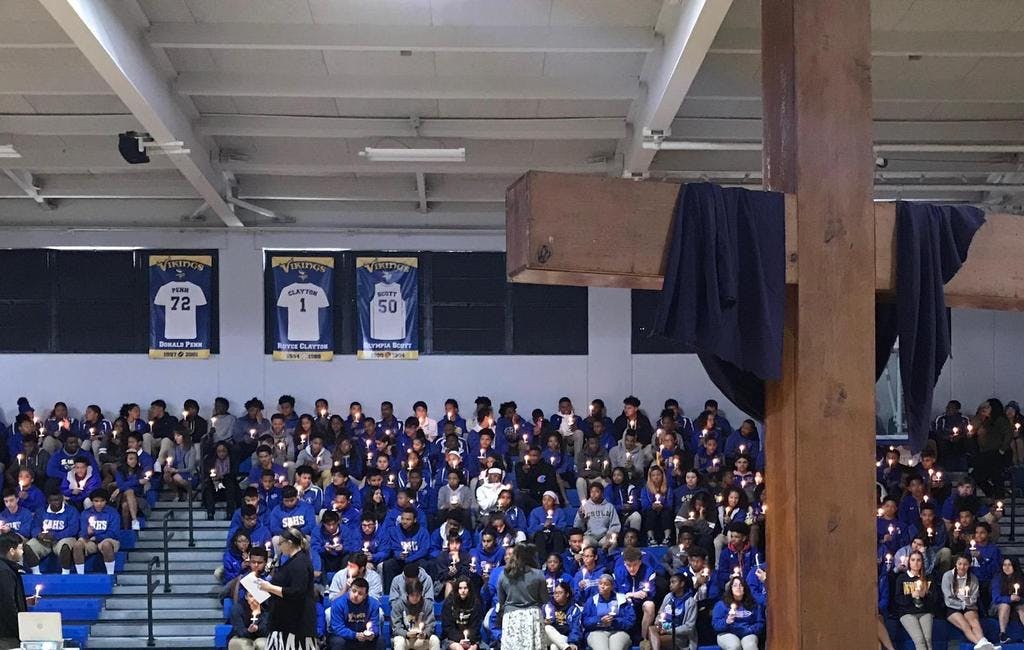 People in bleachers holding candles in a dimly lit gymnasium