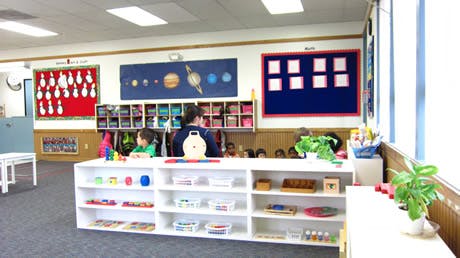 Adult and child in a classroom with shelves and wall decorations