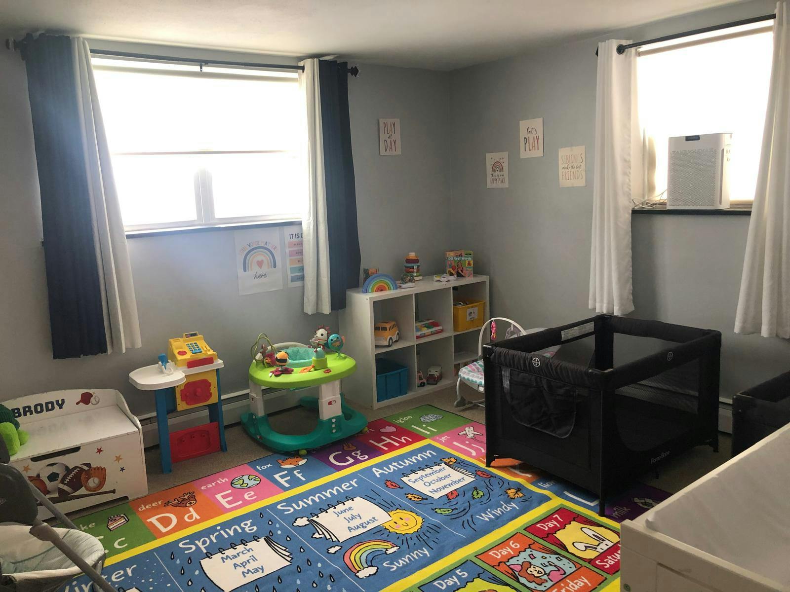 A children's playroom with a colorful alphabet rug, toys, and a portable crib