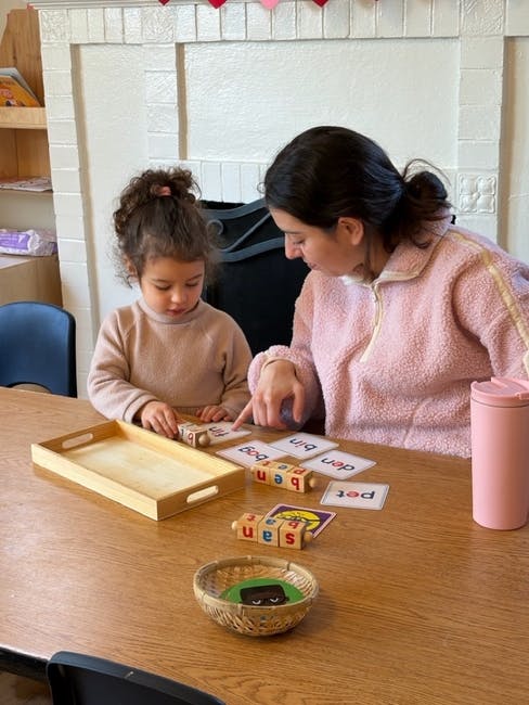 Adult and child playing with letter blocks and word cards on a table