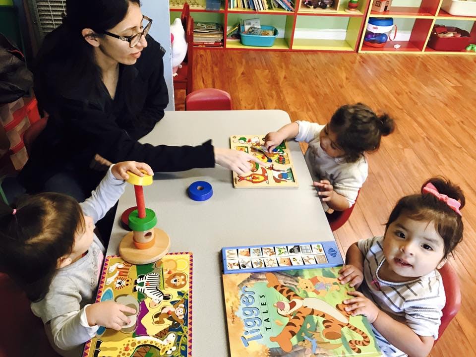 Person and three children playing with puzzles and toys at a table