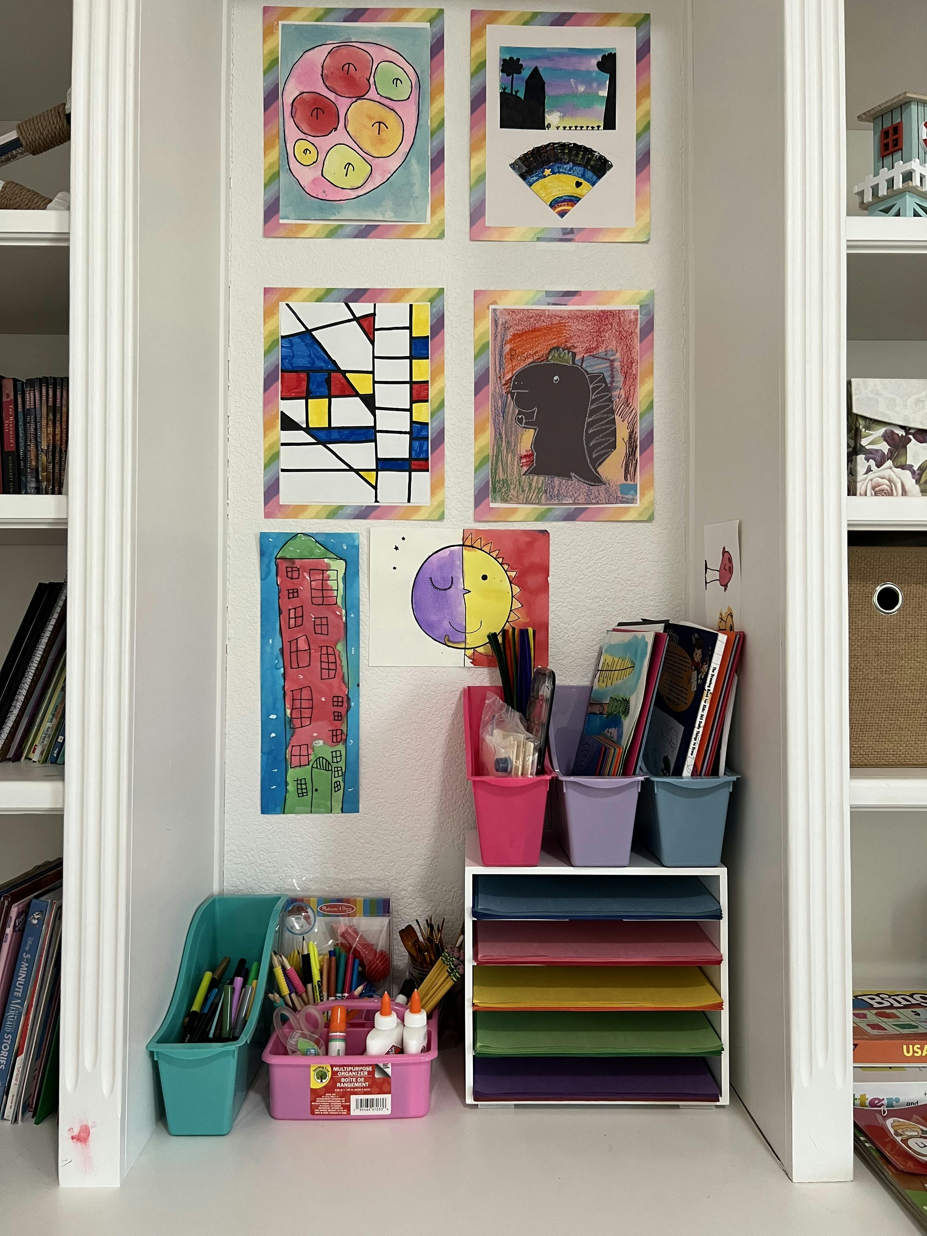 Children's artwork displayed on a wall above art supplies