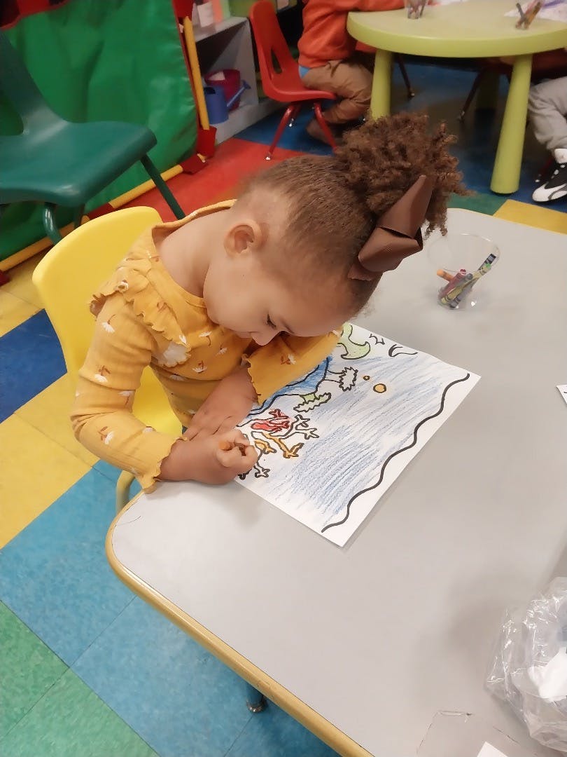 Child coloring on a paper at a desk in a classroom