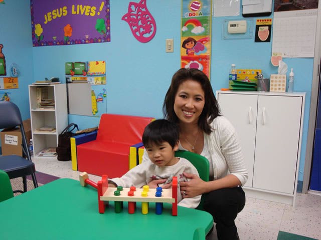 Person and child playing with a toy on a green table in a classroom