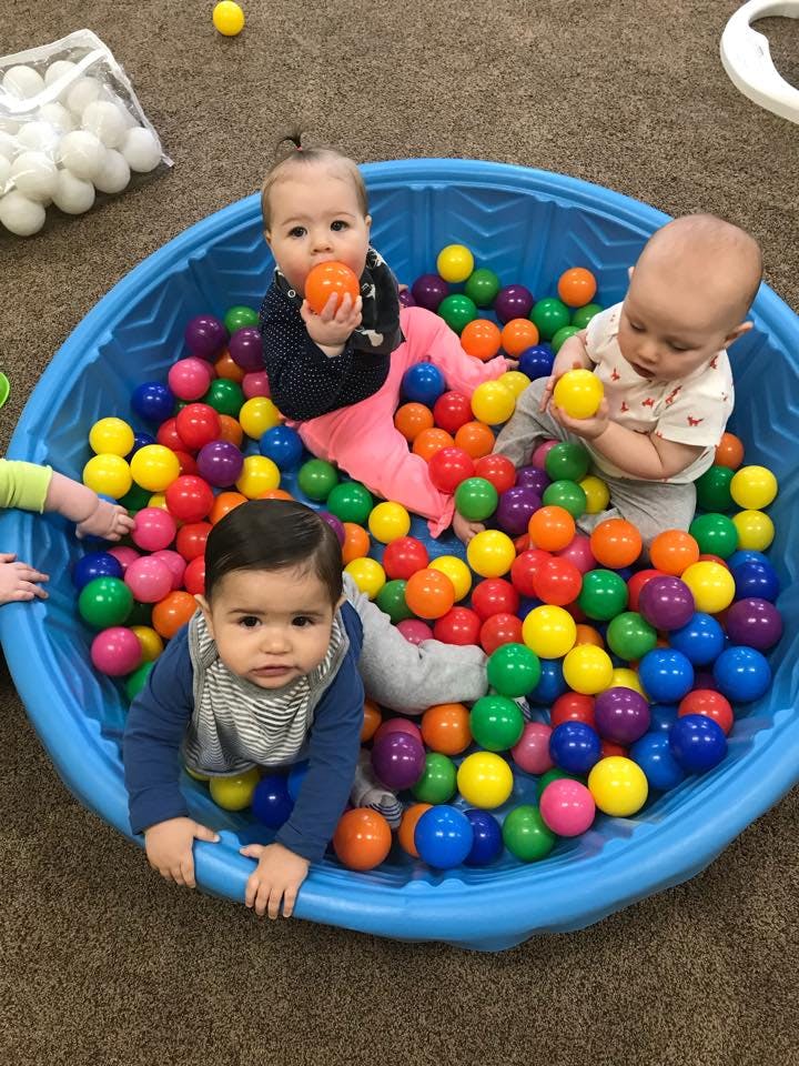 Three children playing in a blue ball pit filled with colorful plastic balls