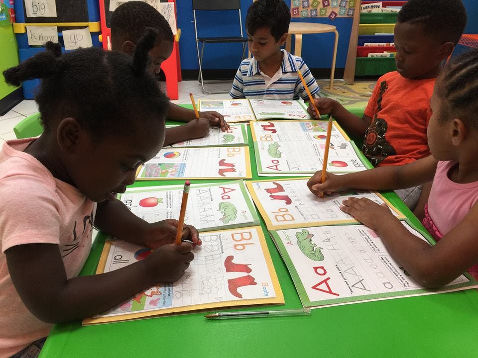 Children writing on alphabet worksheets in a classroom