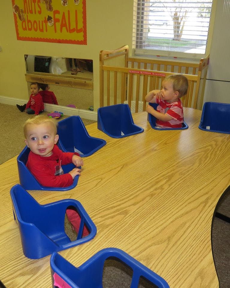 Two children sitting in blue seats at a table in a classroom