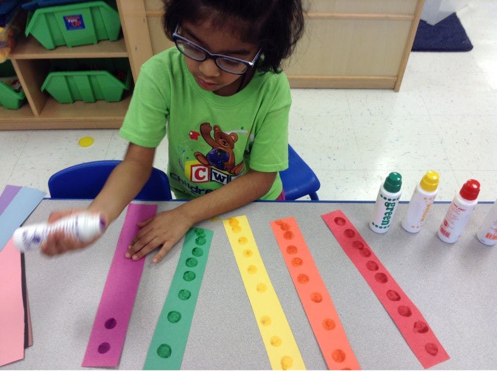 Child applying glue to colorful paper strips with holes