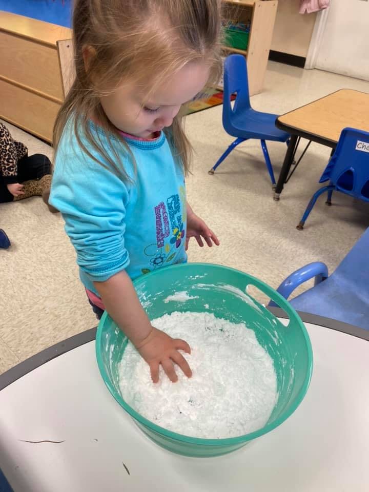 Child with hand in a bowl of white powder in a classroom