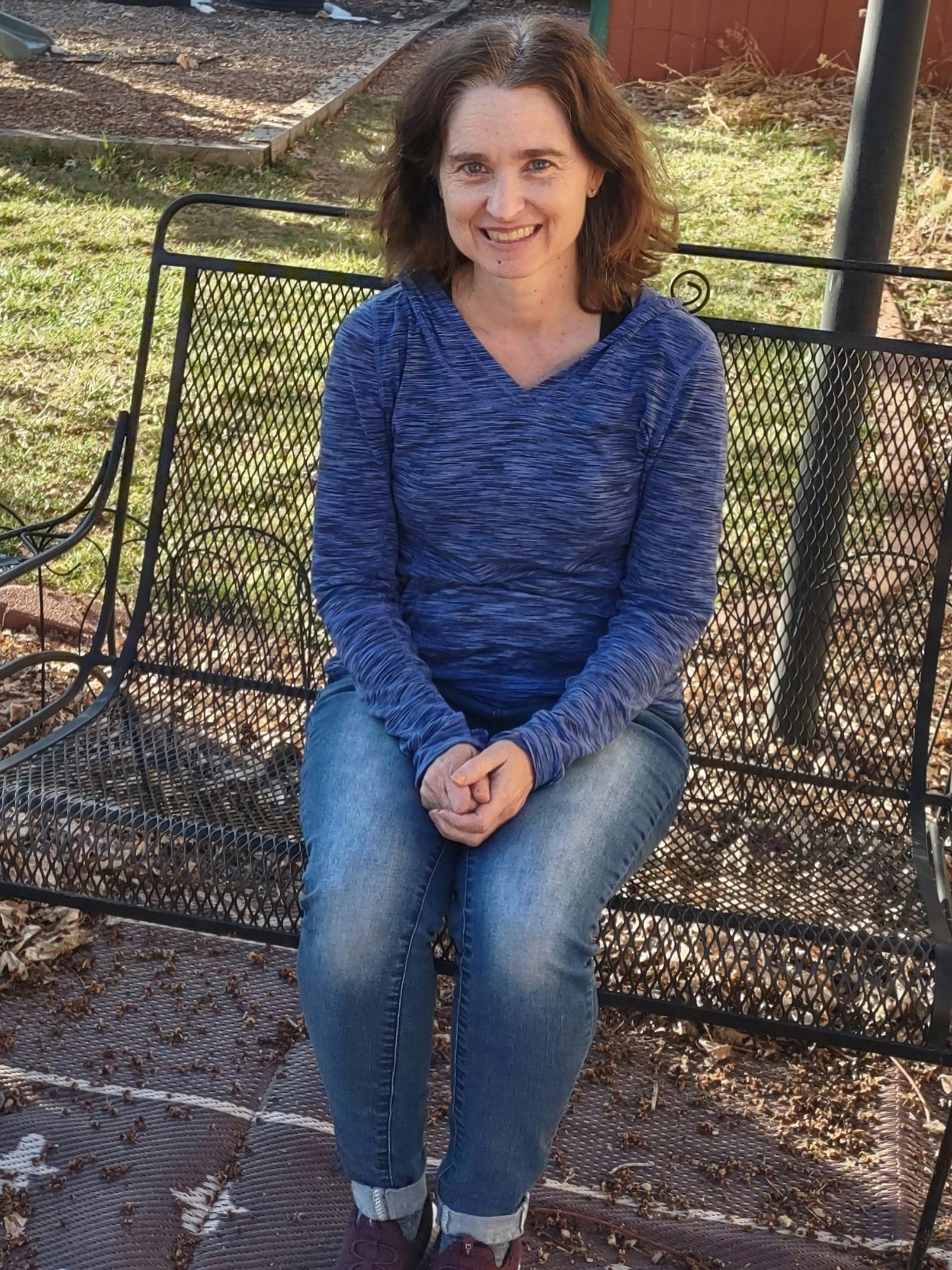 Person with brown hair and a blue shirt sitting on a black metal bench