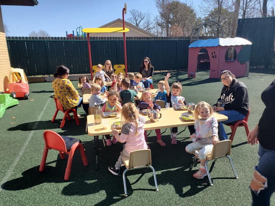 Children and adults sitting at tables outdoors