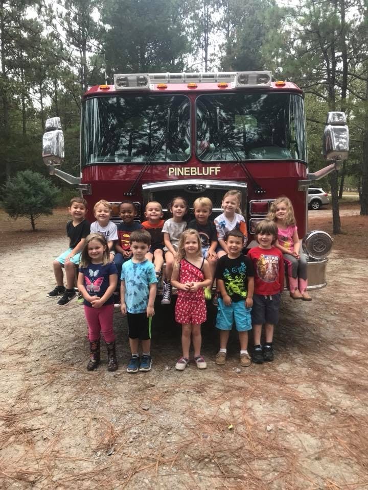 Group of children posing in front of a fire truck with "PINEBLUFF" on the front