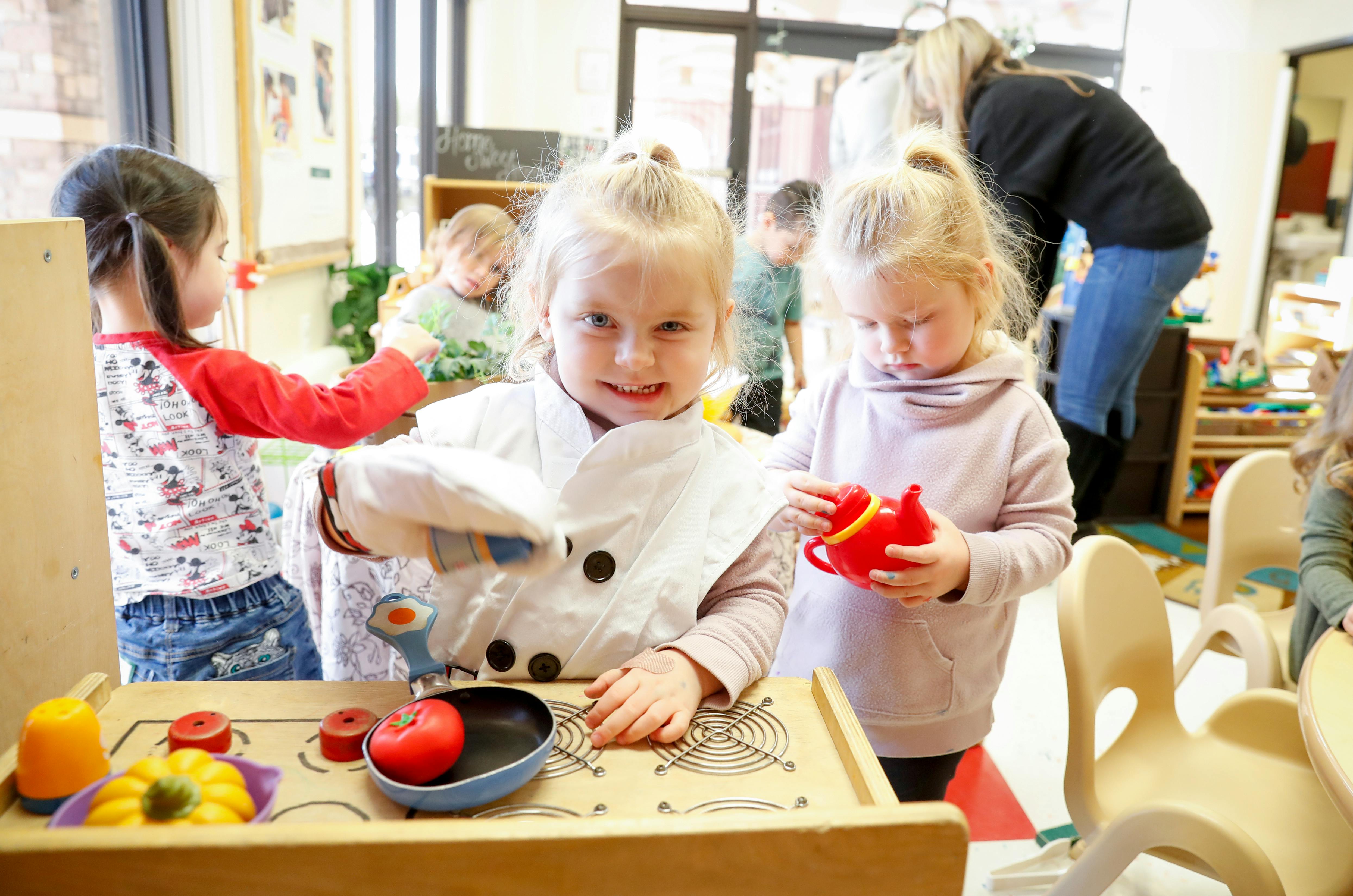 Child in a chef's coat playing with toy food in a classroom