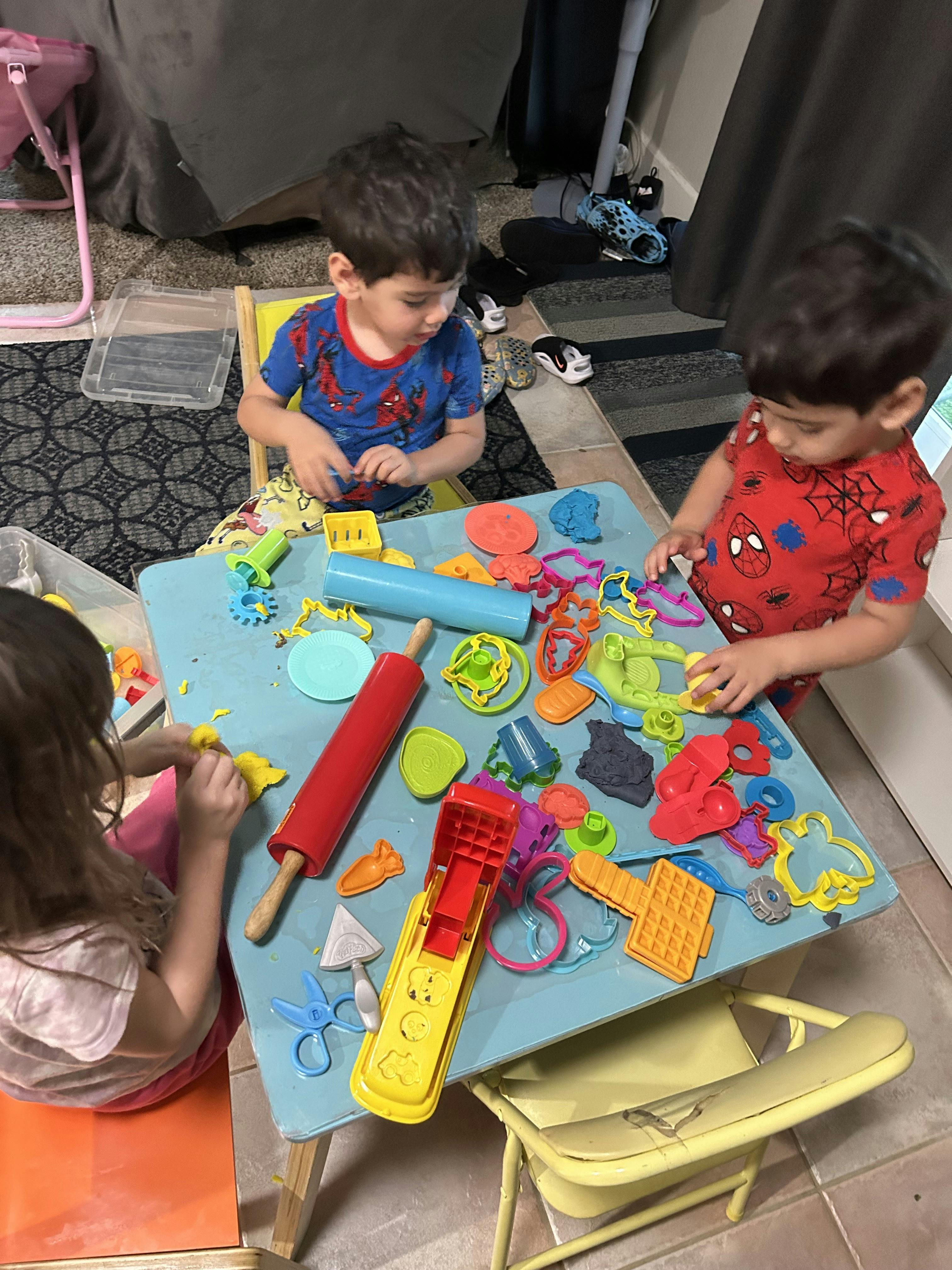 Three children playing with colorful modeling clay and tools at a blue table