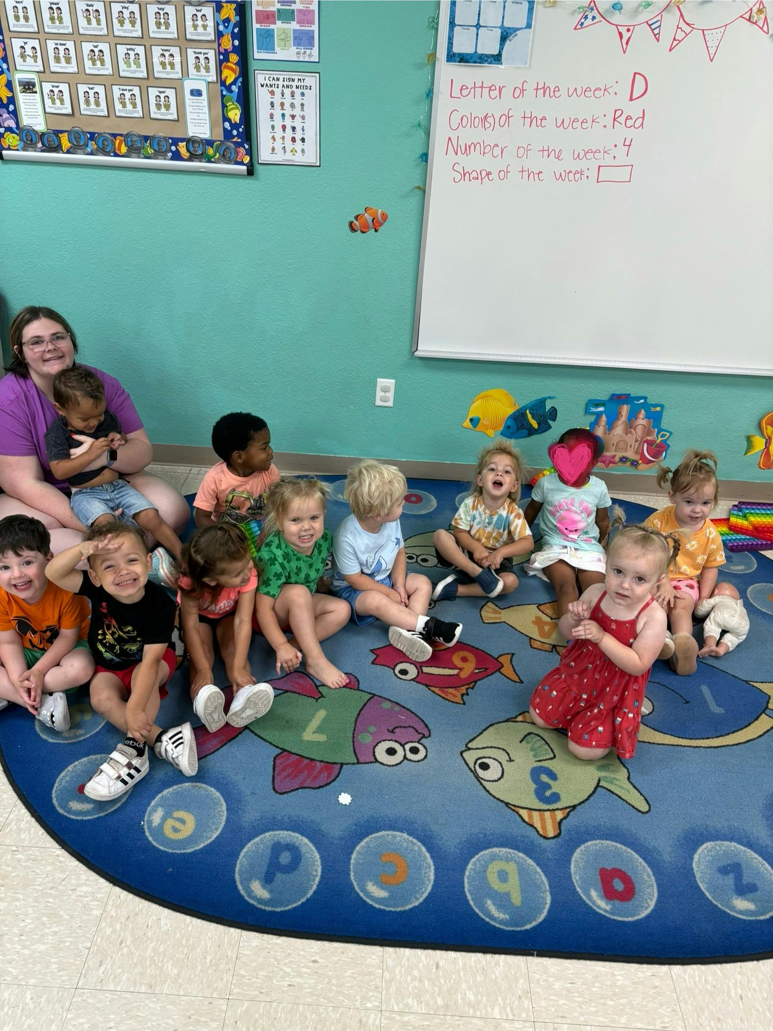 Adult and multiple children sitting on a colorful rug in a classroom