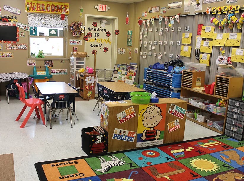Classroom with small tables and chairs, colorful rug, and decorated walls