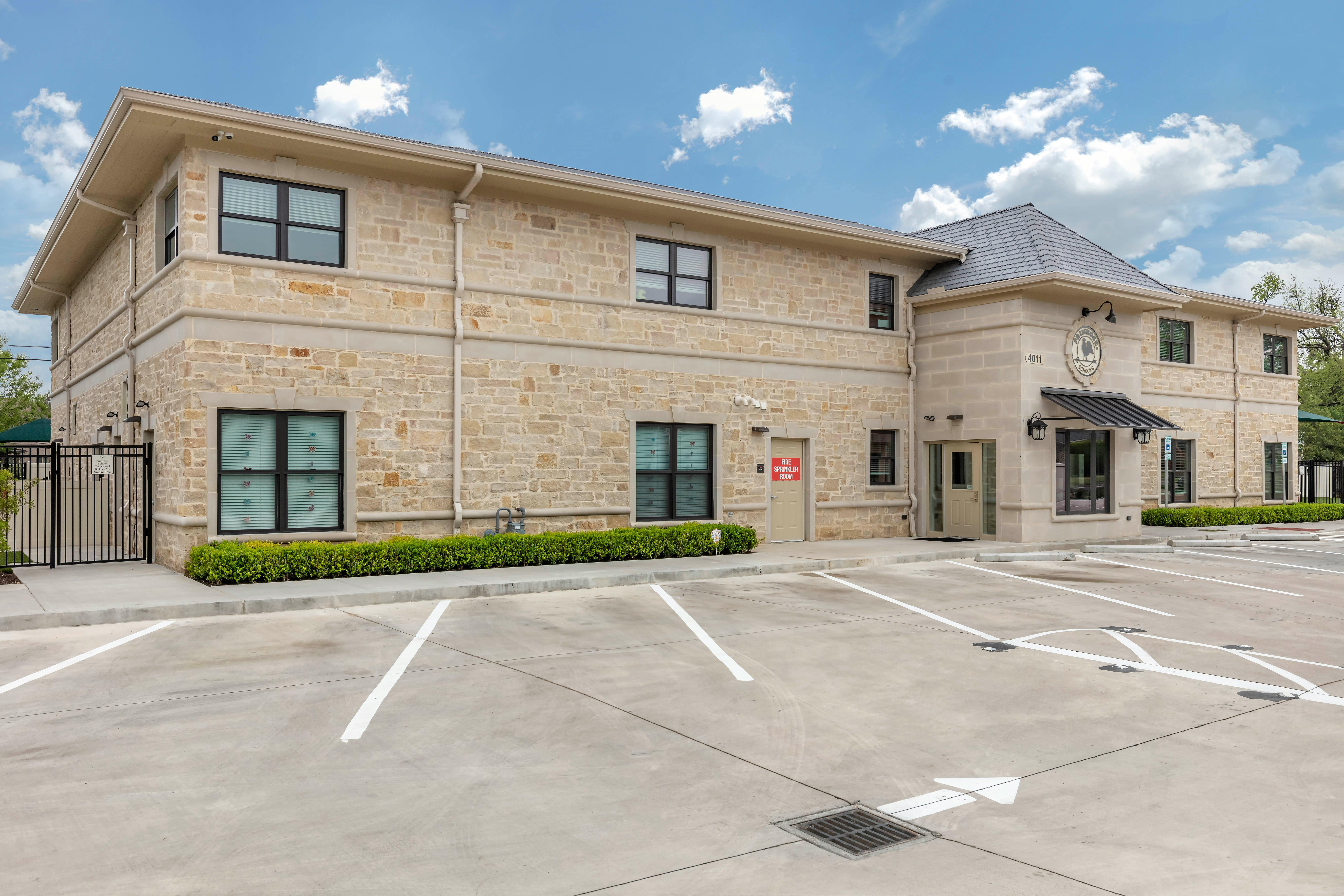 Tan brick building with a dark roof and a parking lot with painted lines