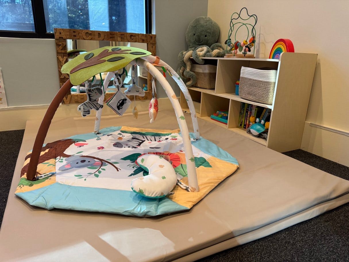A baby play gym with colorful toys on a playmat, surrounded by soft floor mats
