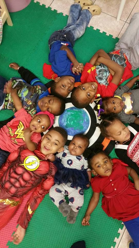 Group of children and babies lying on a green mat, looking up