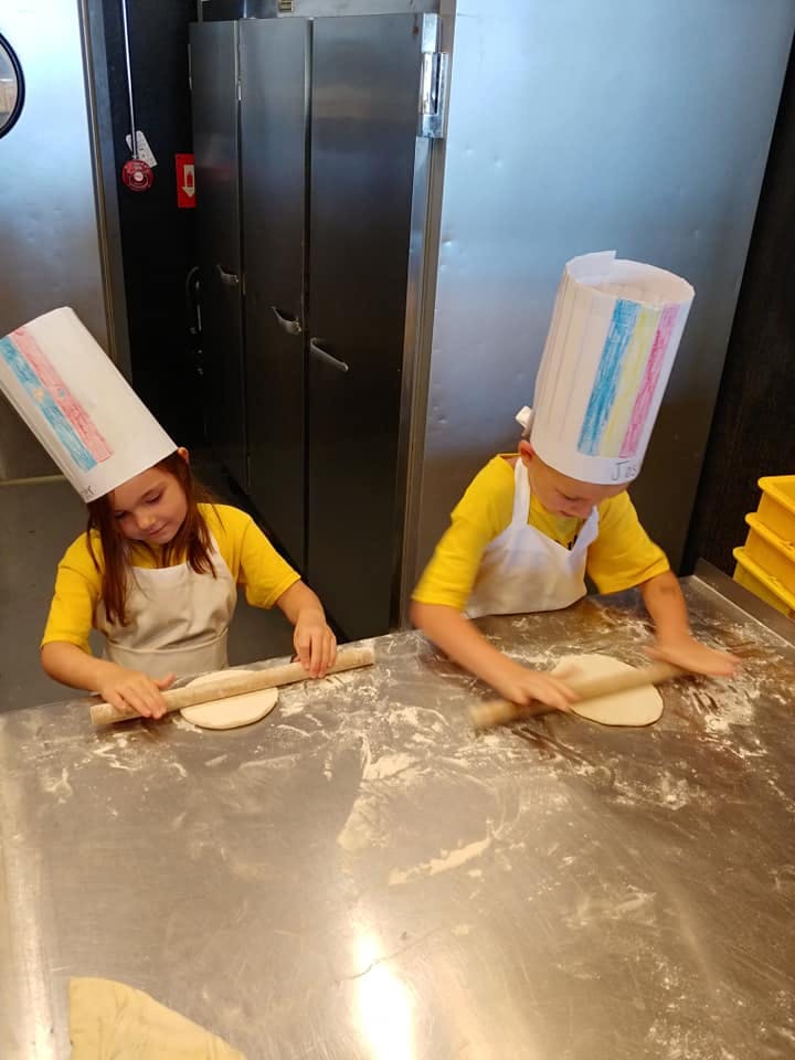 Two children in chef hats and aprons rolling dough with rolling pins