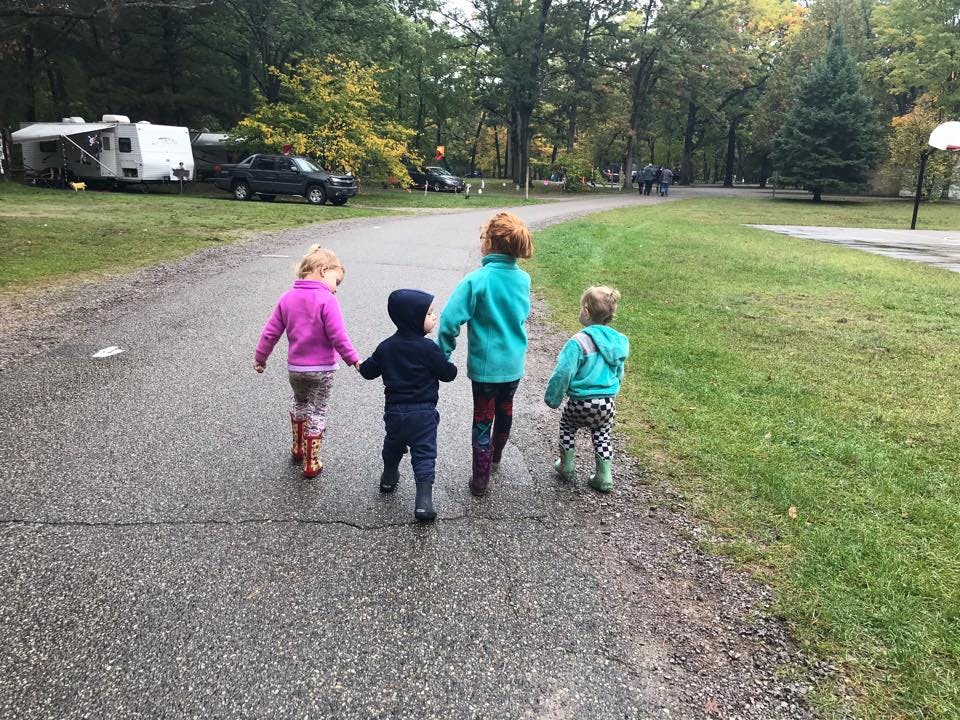 Four children walking on a paved path, tree-lined path
