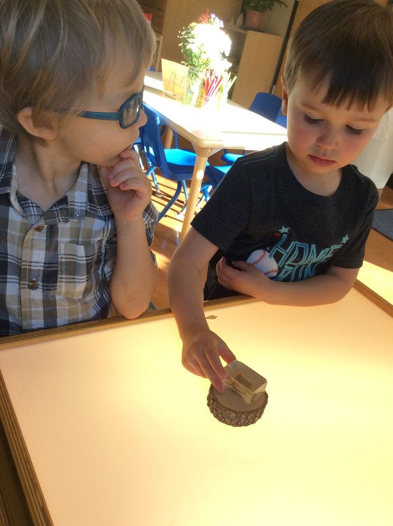 Two children playing with a wooden stamp on a light table