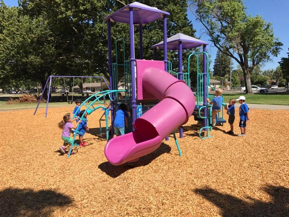 Children playing on a playground with a purple slide and swings