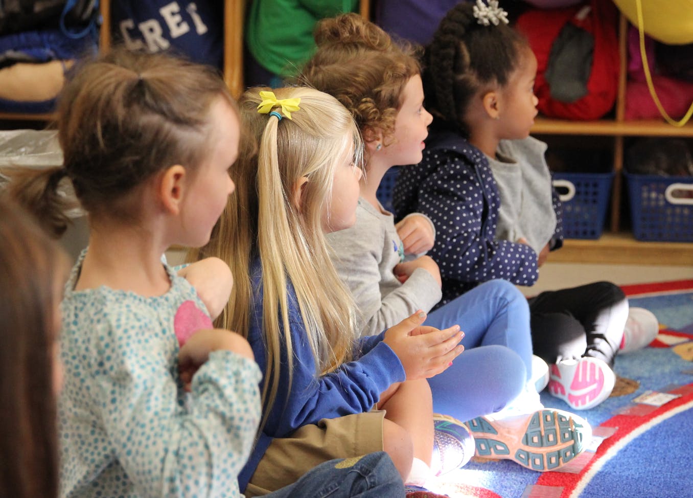 Four children sitting on a rug in a classroom
