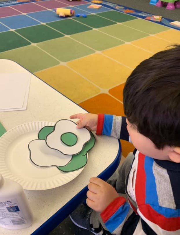 Child making a craft of green eggs on a paper plate