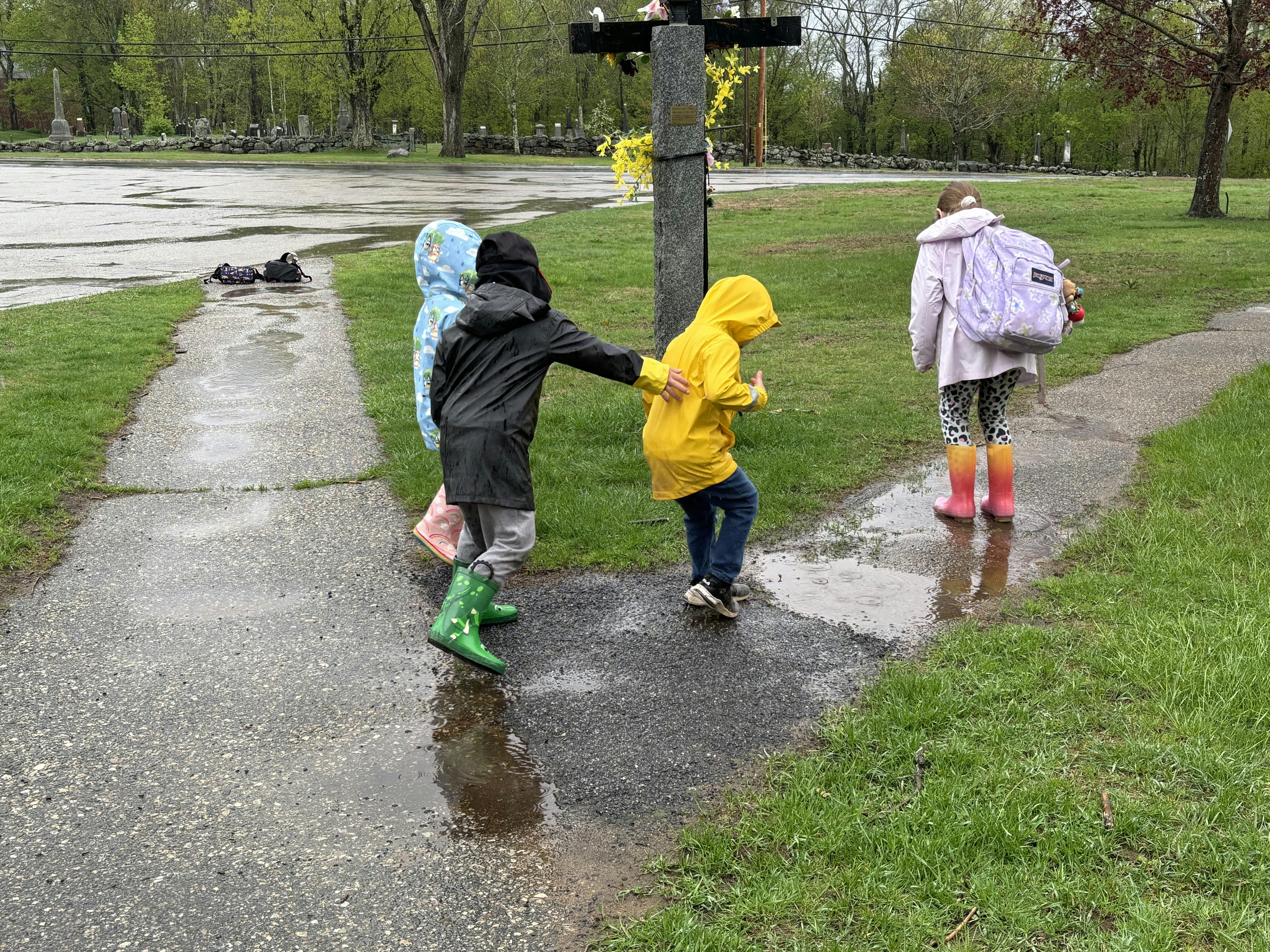 Children in raincoats and boots walking on a wet path