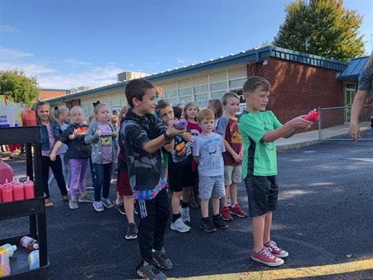 Children in a line holding small objects outdoors
