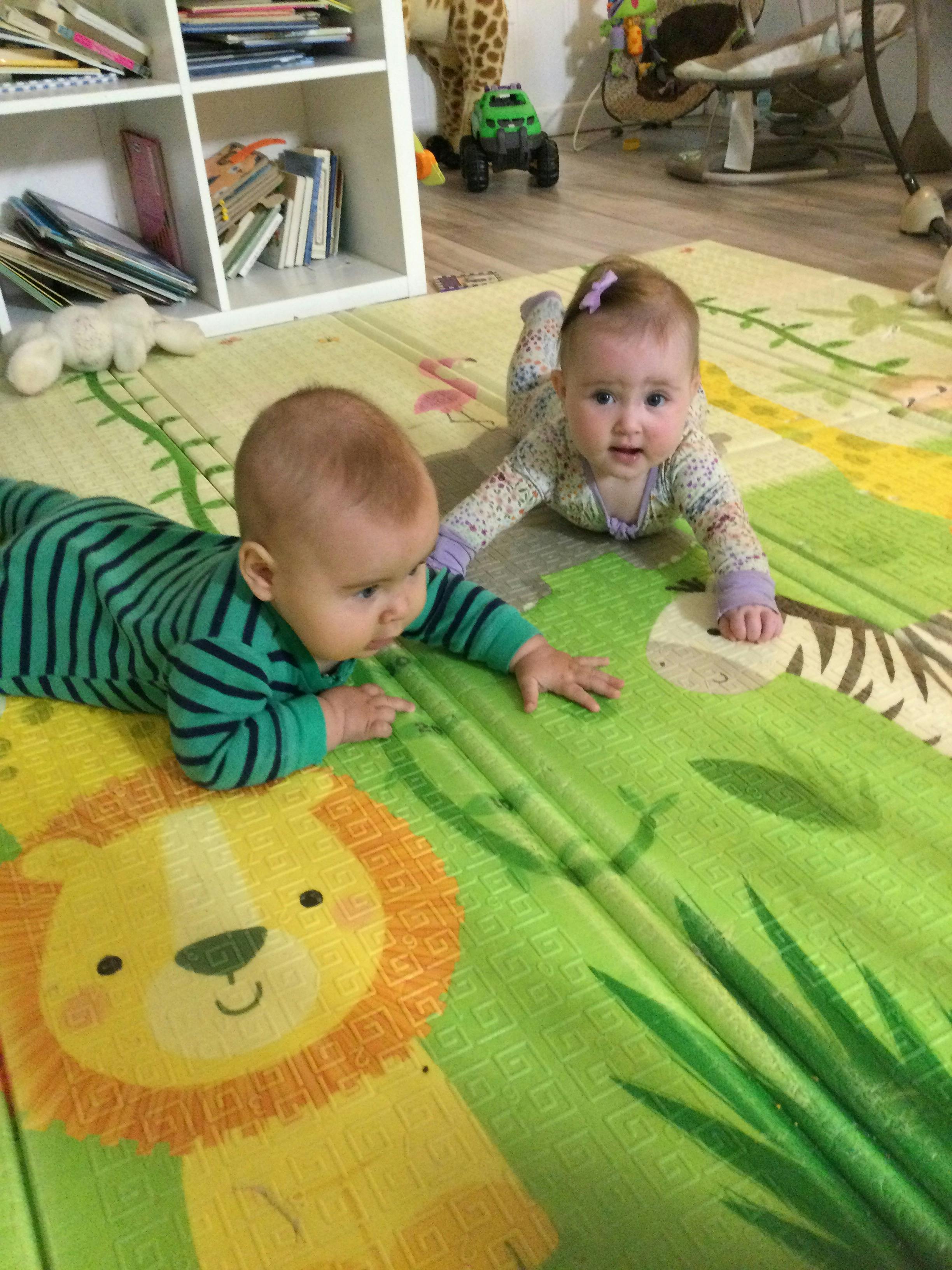 Two babies crawling on a colorful playmat