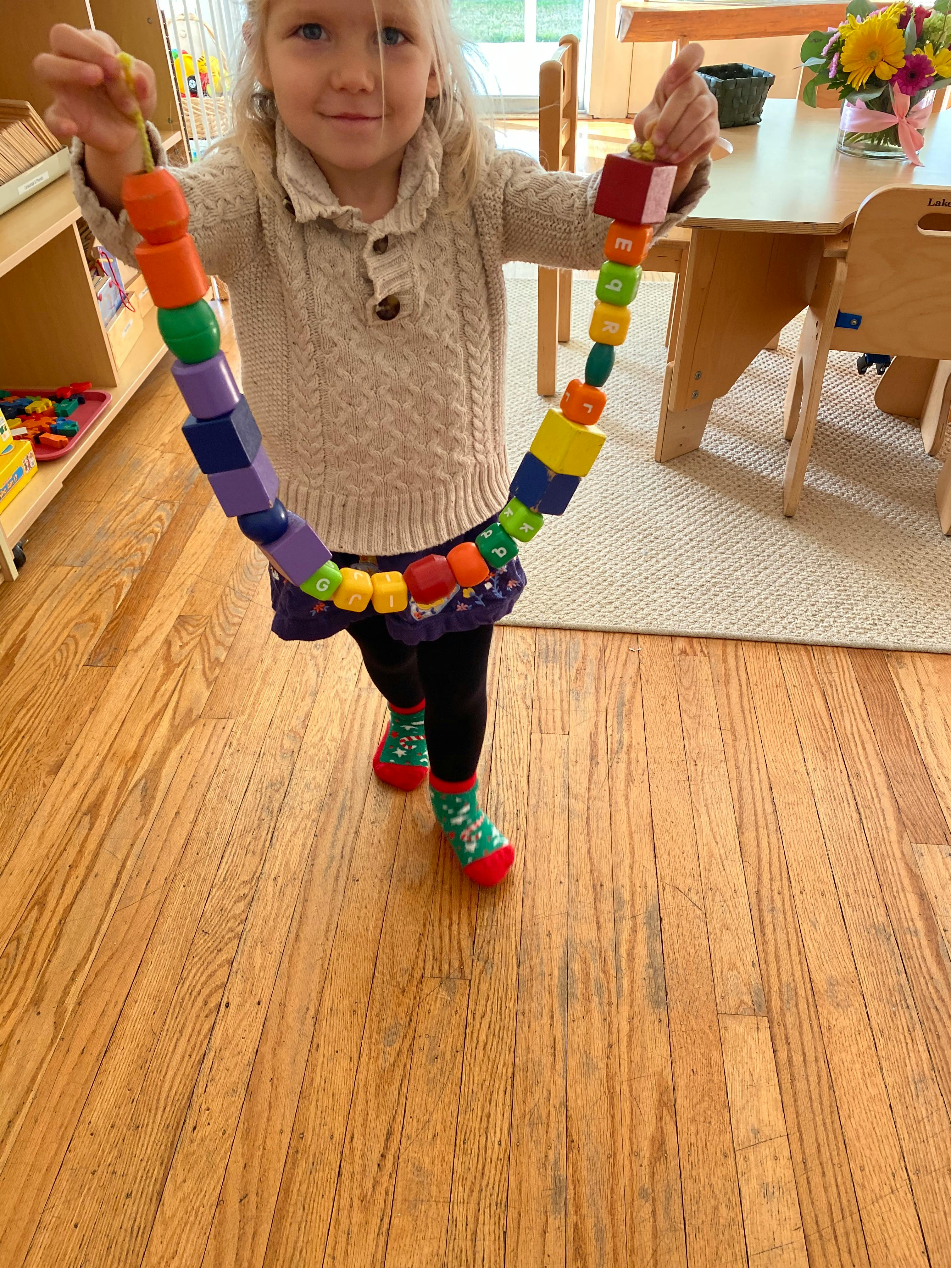 Child holding a long string of colorful wooden beads in a classroom