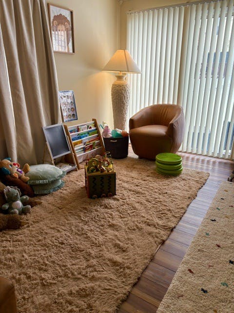 A playroom corner with a shag rug, armchair, toys, and a bookshelf