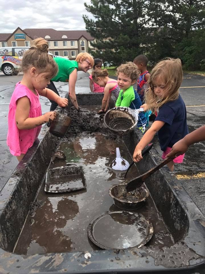 Children playing in a large container of mud with various tools