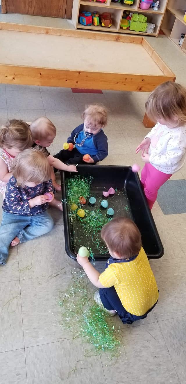 Children playing with plastic eggs and green tinsel in a black bin